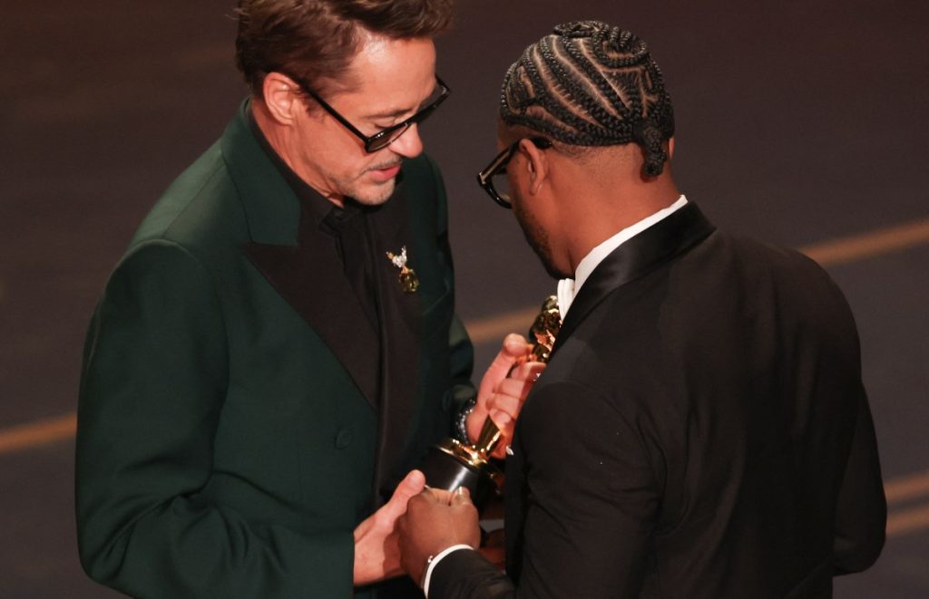 El director y productor de cine estadounidense Ryan Coogler recibe el premio al Mejor Guion Original por "Sinners" de manos del actor estadounidense Robert Downey Jr. (izquierda) en el escenario durante la 98.ª edición de los Premios Óscar en el Dolby Theatre de Hollywood, California, el 15 de marzo de 2026. (Foto de Patrick T. Fallon / AFP)
