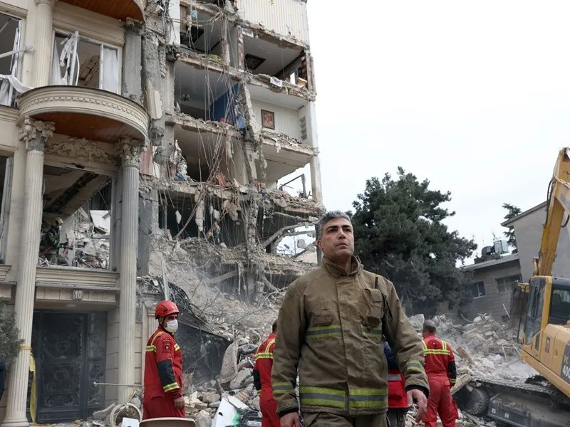 Bomberos y funcionarios iraníes trabajan en el lugar donde se encuentran los edificios residenciales dañados en el norte de Teherán, Irán, el 23 de marzo de 2026.