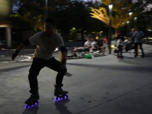 Un patinador practica frenado y control durante una sesión nocturna, mientras otros miembros de la comunidad observan y esperan su turno para entrenar.