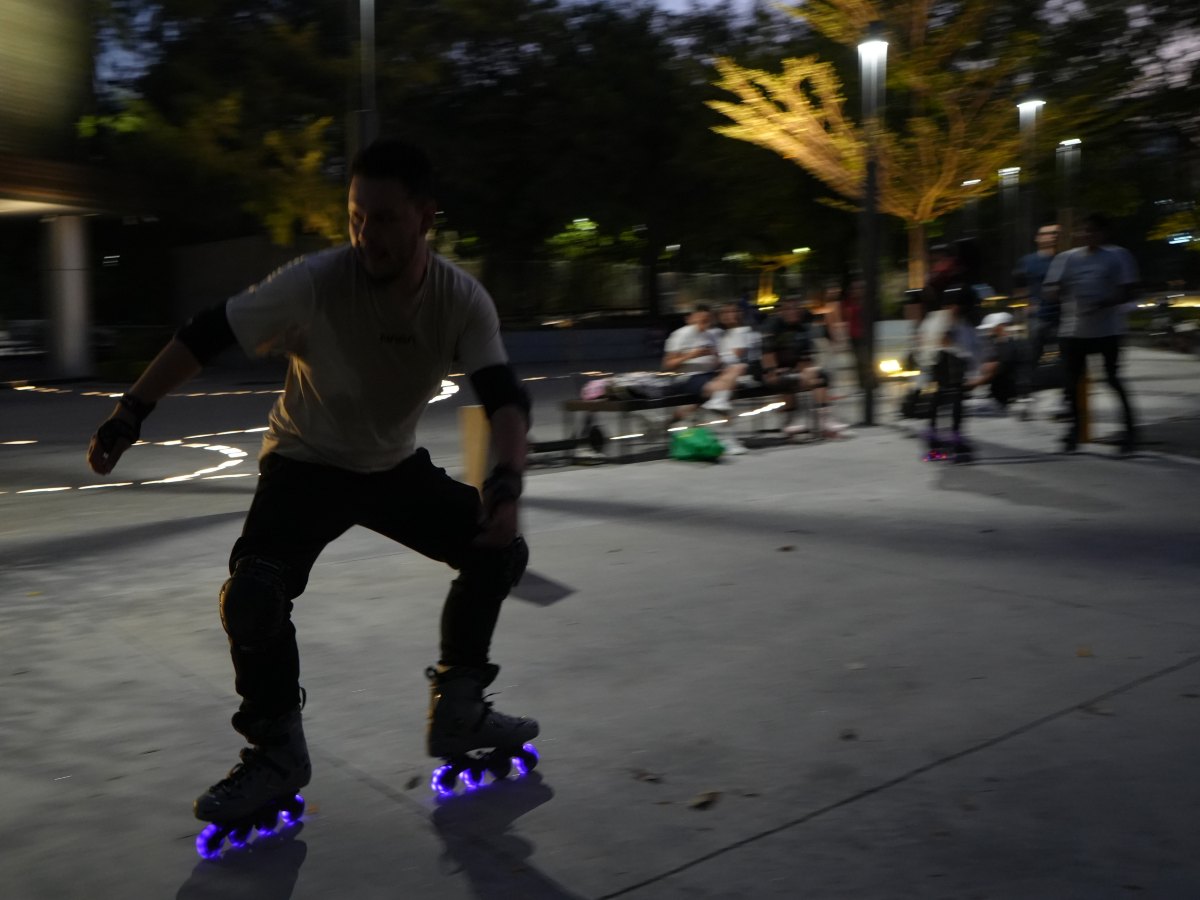 Un patinador practica frenado y control durante una sesión nocturna, mientras otros miembros de la comunidad observan y esperan su turno para entrenar.