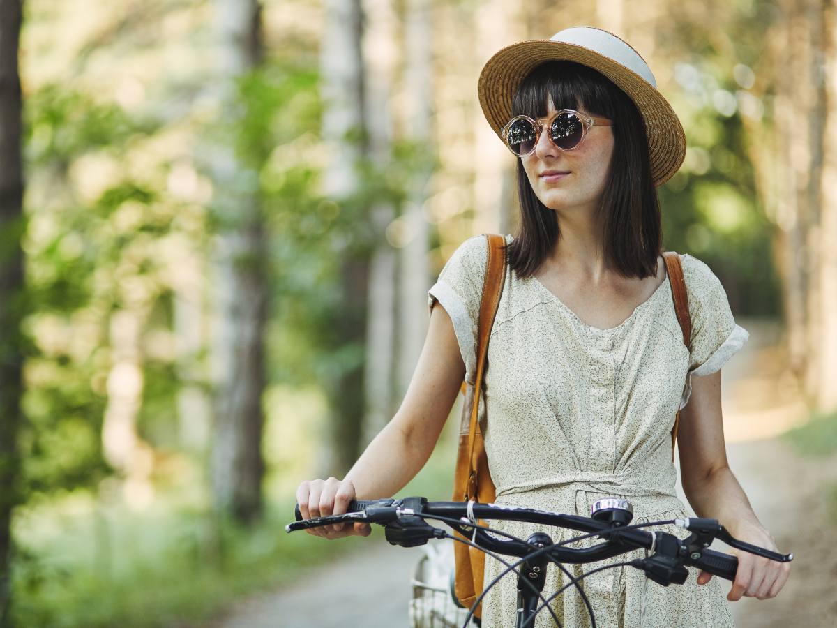 Outdoor fashion portrait of attractive young brunette in a hat on a bicycle.
