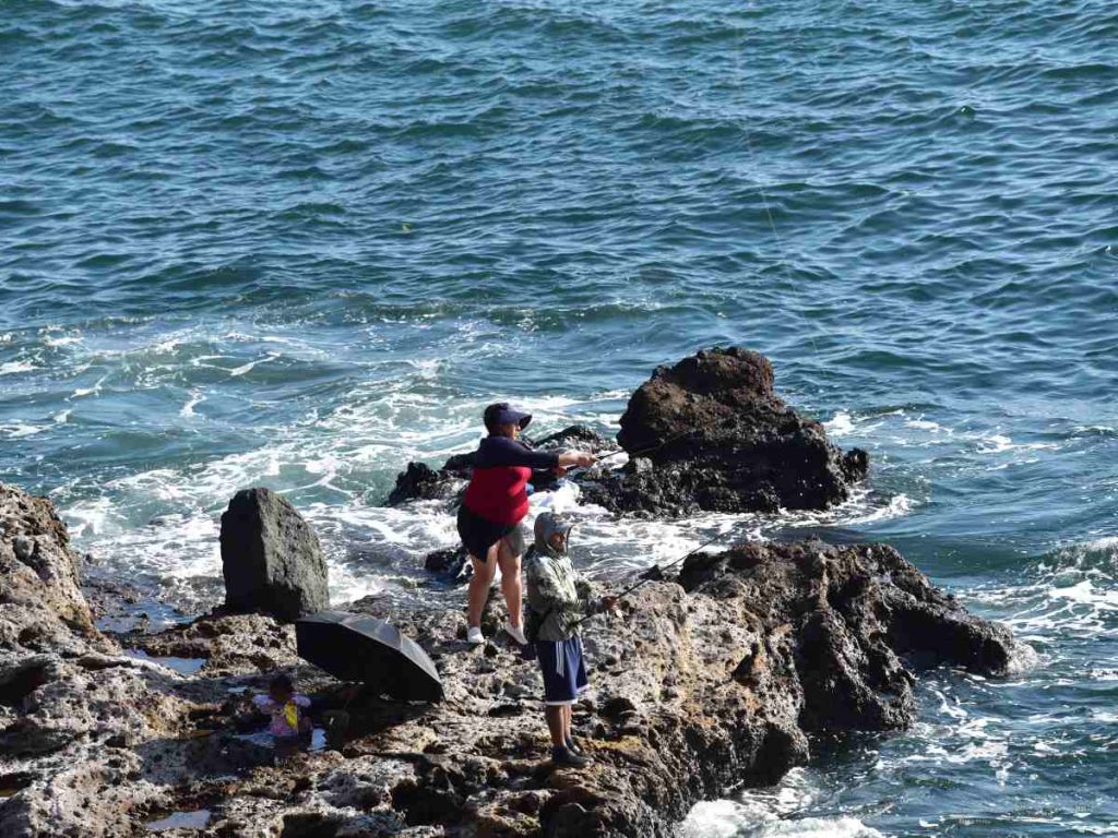 Visitantes practican pesca en las rocas del muelle de Acajutla, una actividad común entre locales y turistas en la zona.