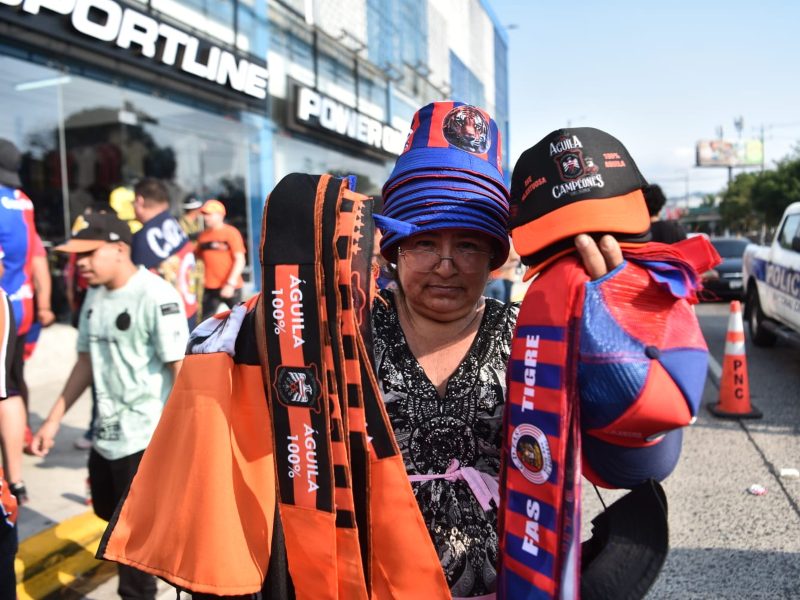 Vendedores aprovechan el ambiente de la final entre FAS y Águila para ofrecer banderas, camisetas y comida en los alrededores del “Mágico” González.