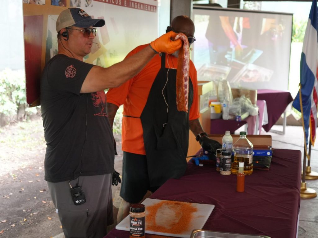 Bob Trudnak muestra costillas sazonadas durante la demostración de barbacoa estadounidense junto a Moe Cason.