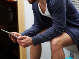 Man with touchpad networking while sitting on toilet-bowl