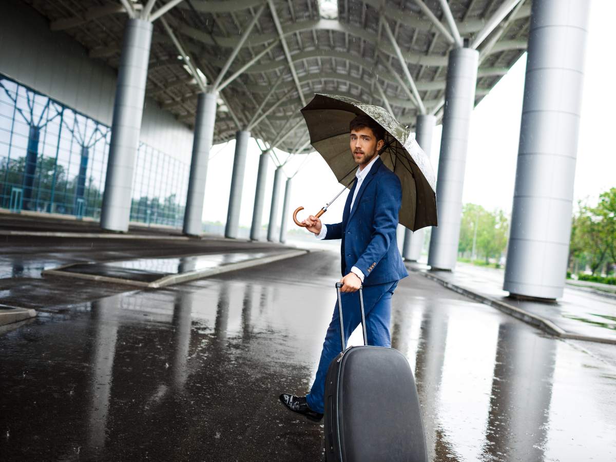Picture of  young  businessman holding  suitcase and umbrella walking in rain