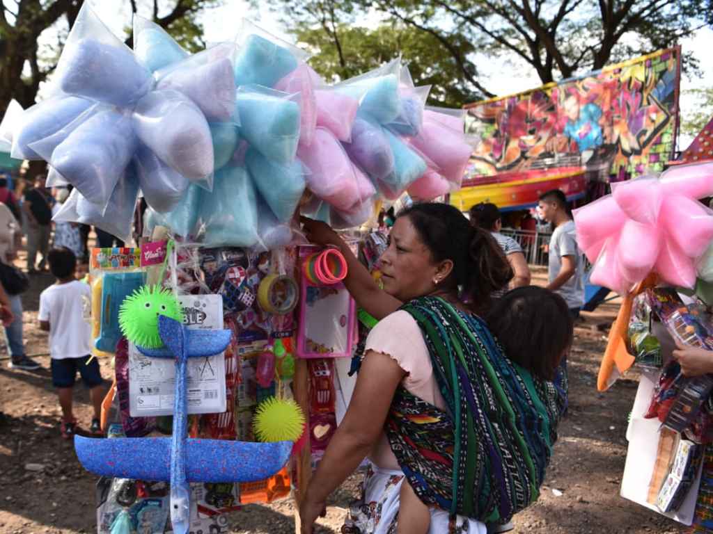 Vendedora de algodón de azúcar y juguetes con un bebé a la espalda.s