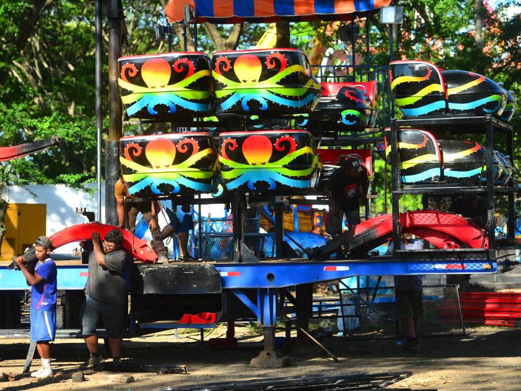 Vista del juego mecánico familiar "El Pulpo" en pleno funcionamiento en el Campo de la Feria de las Fiestas Julias. Sus coloridos brazos metálicos giran de forma moderada elevando los carritos donde viajan adultos y niños sonrientes. El entorno refleja un ambiente festivo y familiar bajo la luz del día, con otras atracciones de fondo.
