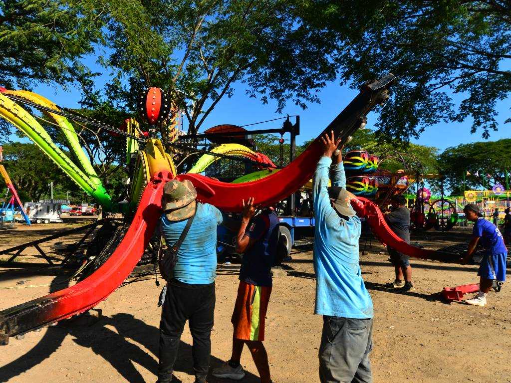 Varios operarios y técnicos trabajan en el ensamblaje de la atracción mecánica "El Pulpo" en un terreno de tierra del Campo de la Feria