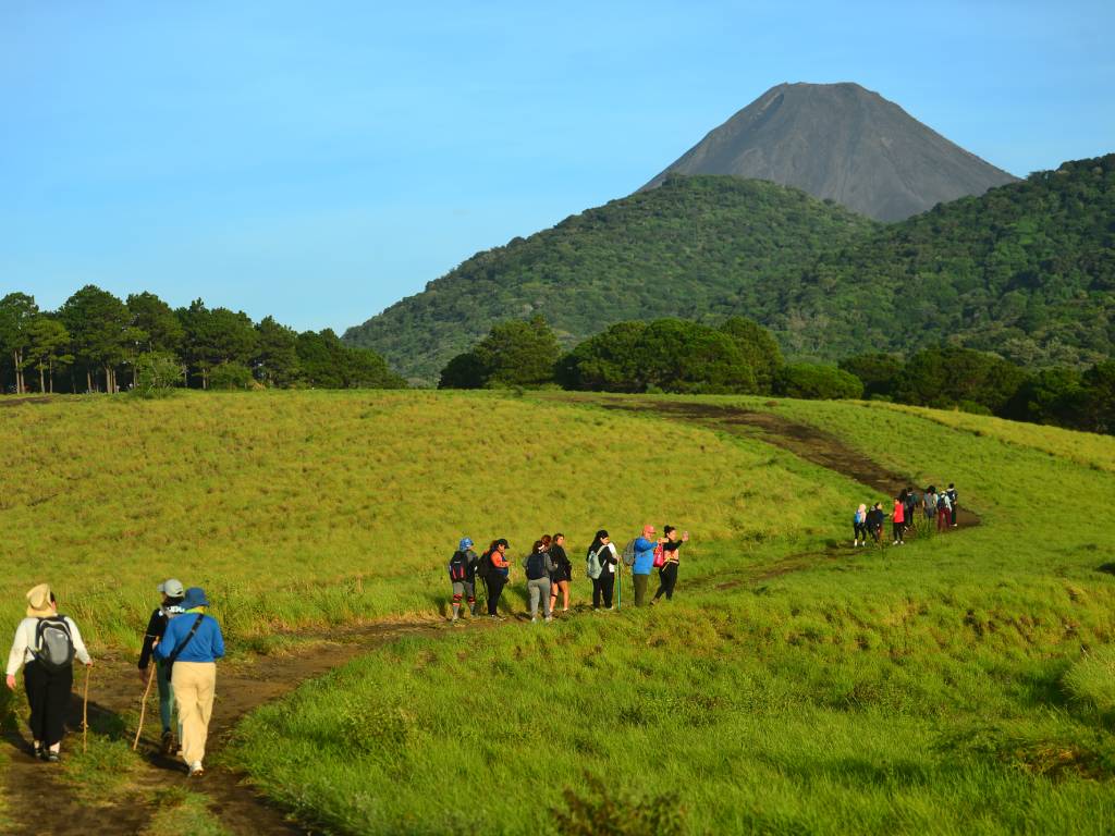 SIGUIENDO EL SENDERO HACIA EL GIGANTE Paso a paso, el grupo de Rumbo Femenino recorre los senderos a la altura del Cerro El Chino, en Sonsonate. Esta ruta ofrece una vista espectacular: el imponente y legendario Volcán de Izalco recortado contra un cielo azul perfecto. Una caminata llena de verde, historia y la mejor energía compartida. ¡Naturaleza en su máxima expresión!