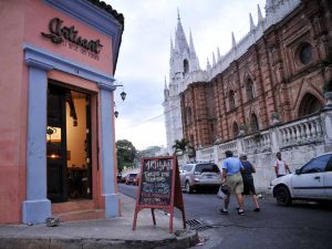 Una toma de esquina de la colorida fachada del restaurante Artisant en Santa Ana. La pared de estuco rosa tiene un letrero negro con la frase 
