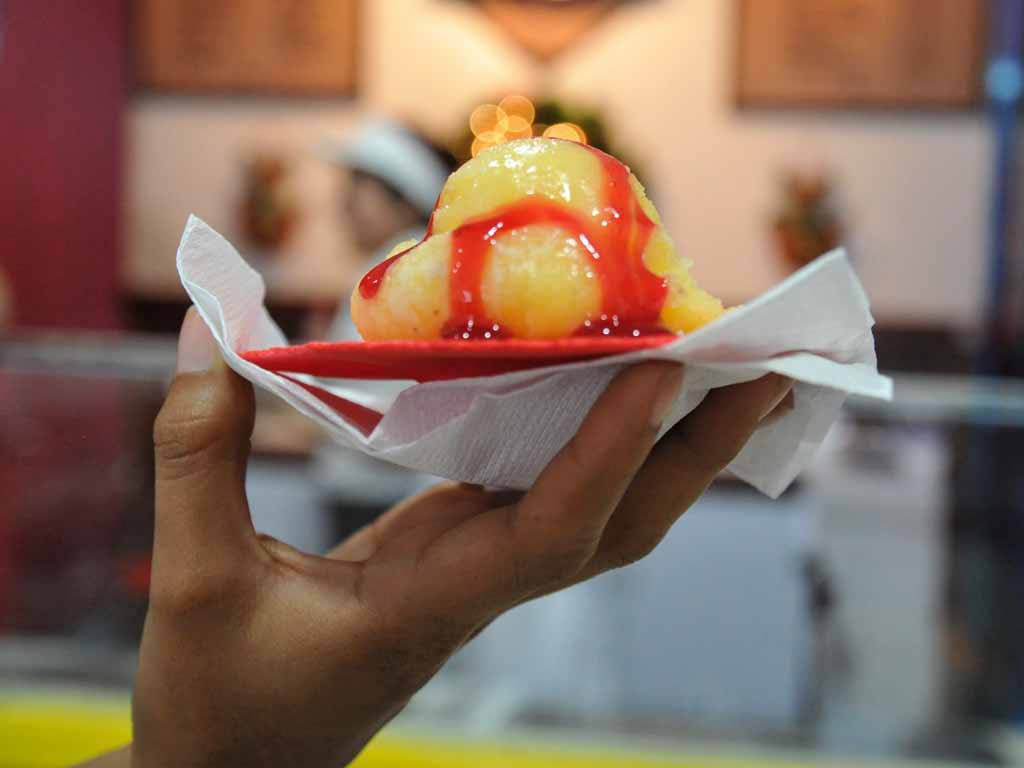 Mano sosteniendo un sorbete de coco bañado con jalea roja de fresa.