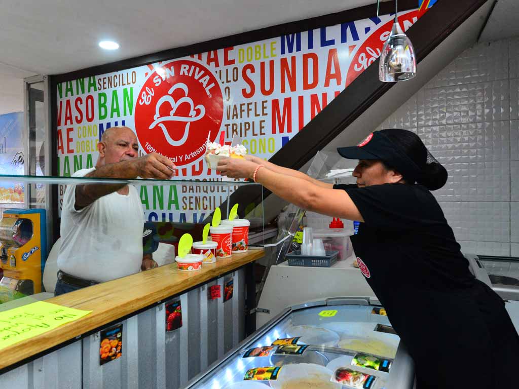Empleada entregando un helado artesanal a un cliente en el mostrador.