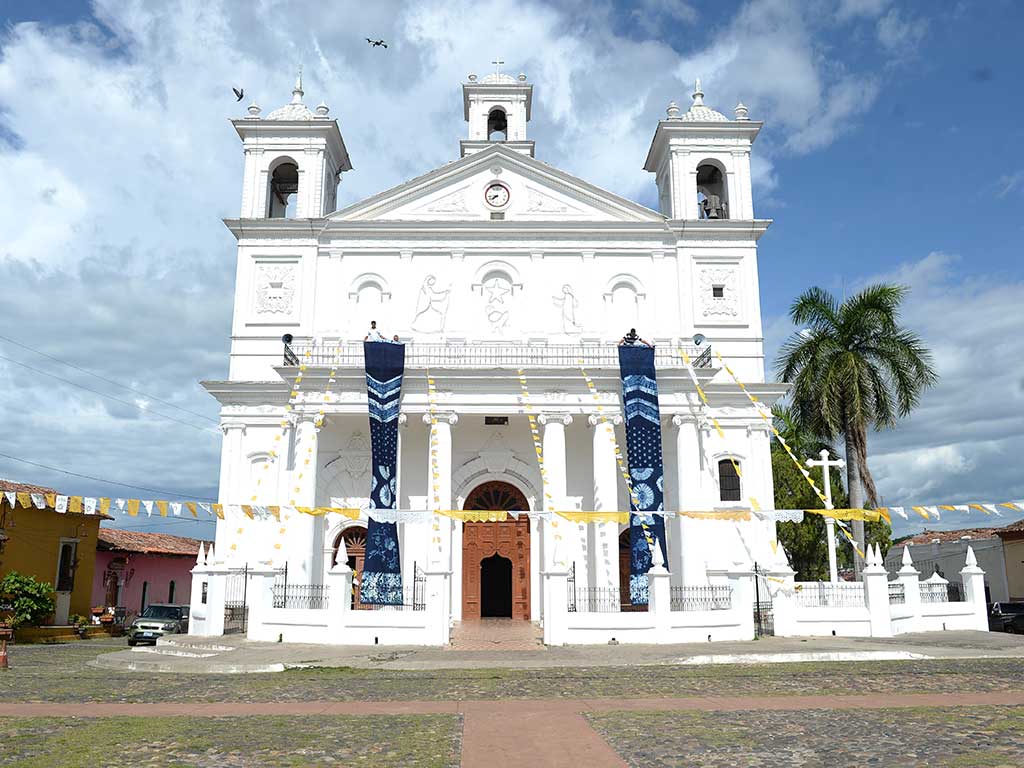 Fachada de la iglesia de Suchitoto con largos lienzos azules teñidos de añil colgando de su balcón.