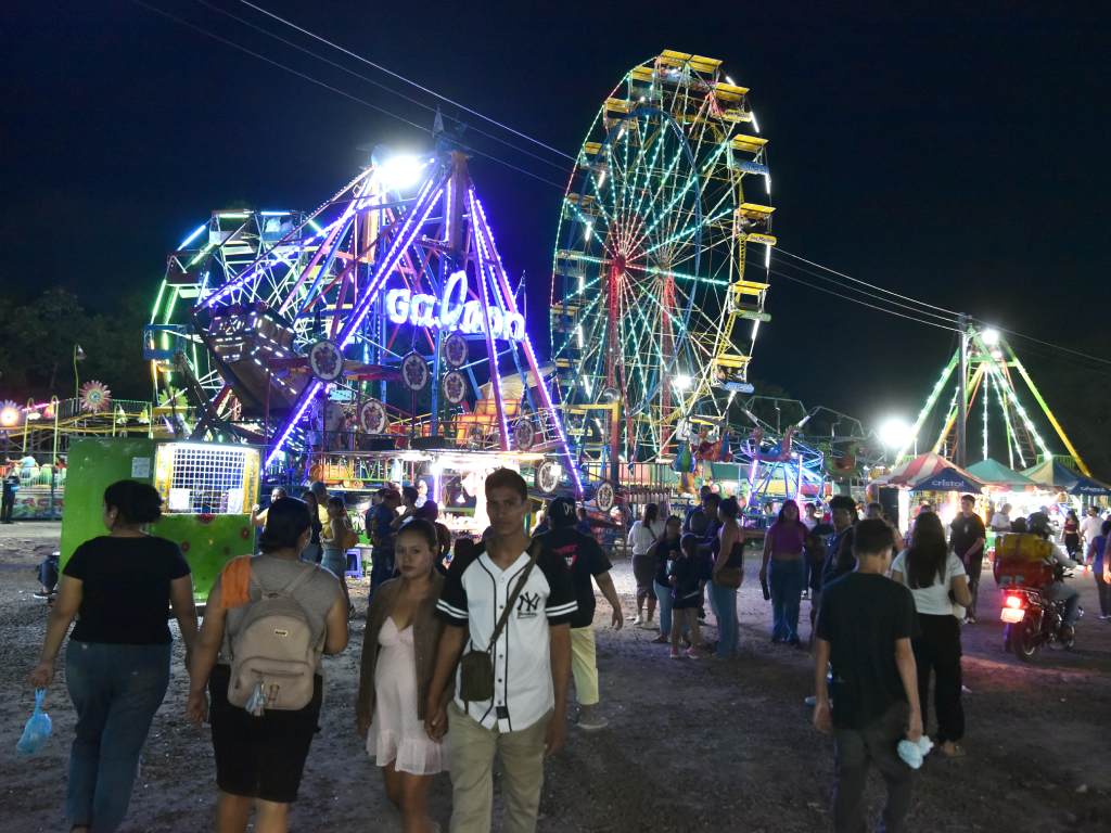 Una vista panorámica de la feria nocturna, llena de luces brillantes y gente paseando.
