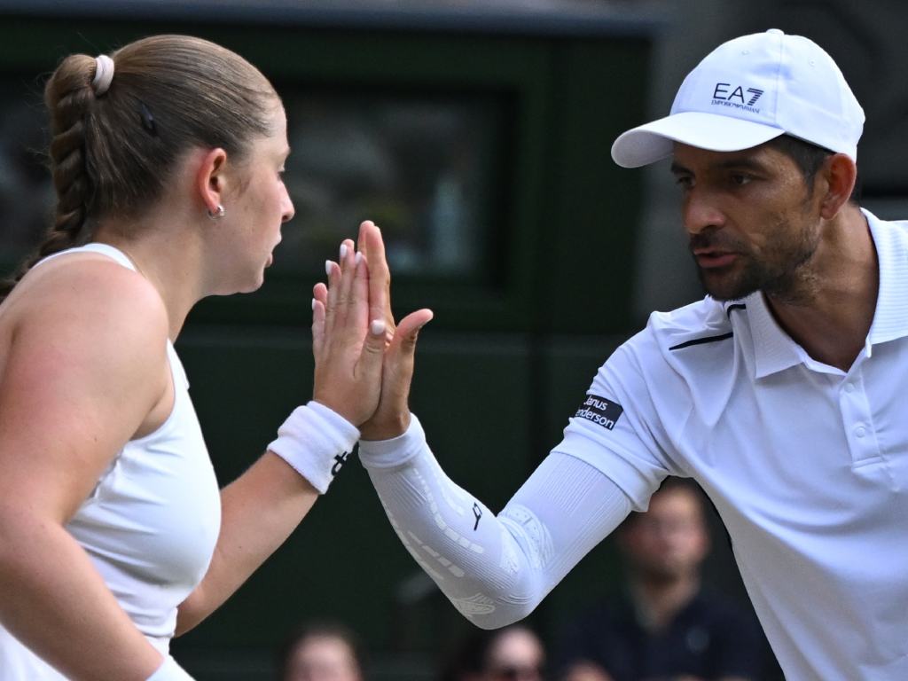 Un plano medio muy cercano que captura un momento de comunicación y choque de manos ("high-five") entre Ostapenko y Arévalo. Mientras chocan las palmas para celebrar un punto o darse ánimos, Arévalo le habla de cerca a su compañera con una expresión de total concentración y determinación. La química y el trabajo en equipo quedan perfectamente retratados aquí.