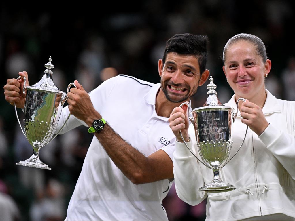 La foto perfecta para cerrar. Marcelo Arévalo y Jelena Ostapenko posan juntos, muy sonrientes y orgullosos, sosteniendo los icónicos trofeos plateados que los acreditan como los flamantes campeones de dobles mixtos del torneo. Arévalo muestra una divertida expresión de felicidad y asombro, mientras Ostapenko sonríe con dulzura a la cámara tras haber alcanzado la gloria en la catedral del tenis.