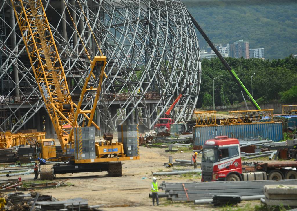 Vista de cerca de grúas y excavadoras operando sobre el terreno de tierra dentro de la zona de construcción del estadio.