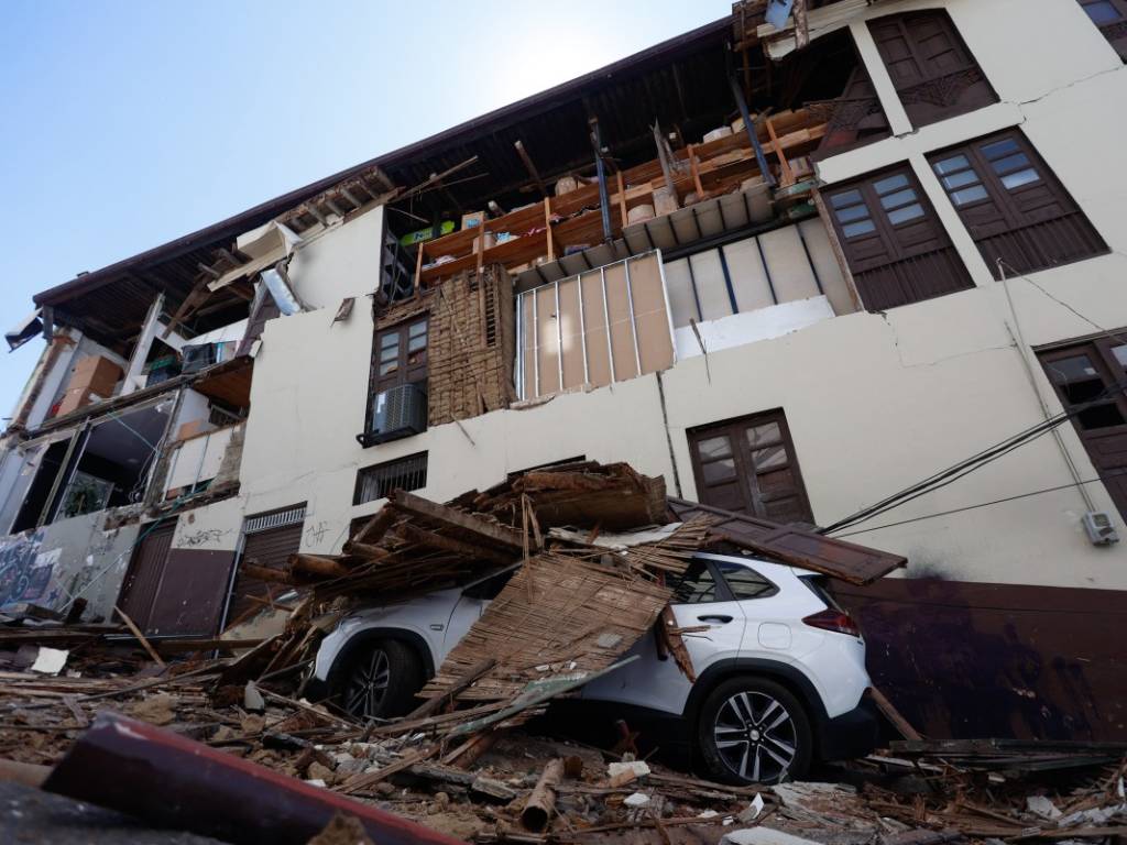 Vista de una fachada dañada y un automóvil cubierto de escombros en Manizales.