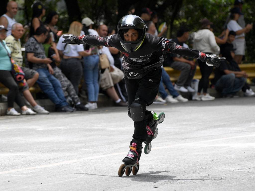 Patinador profesional en línea desciende por una calle, con casco negro y equipo de protección, manteniendo el equilibrio con los brazos extendidos.