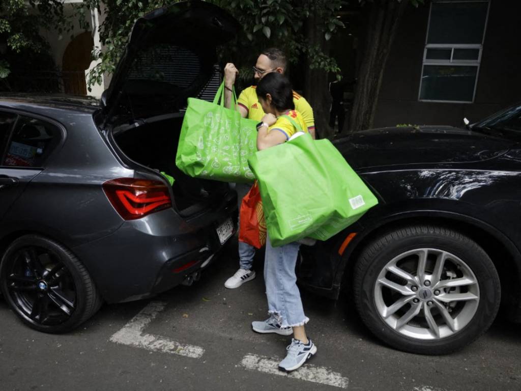 Dos personas con camisetas amarillas de Colombia cargan bolsas verdes con donaciones en la cajuela de un automóvil.