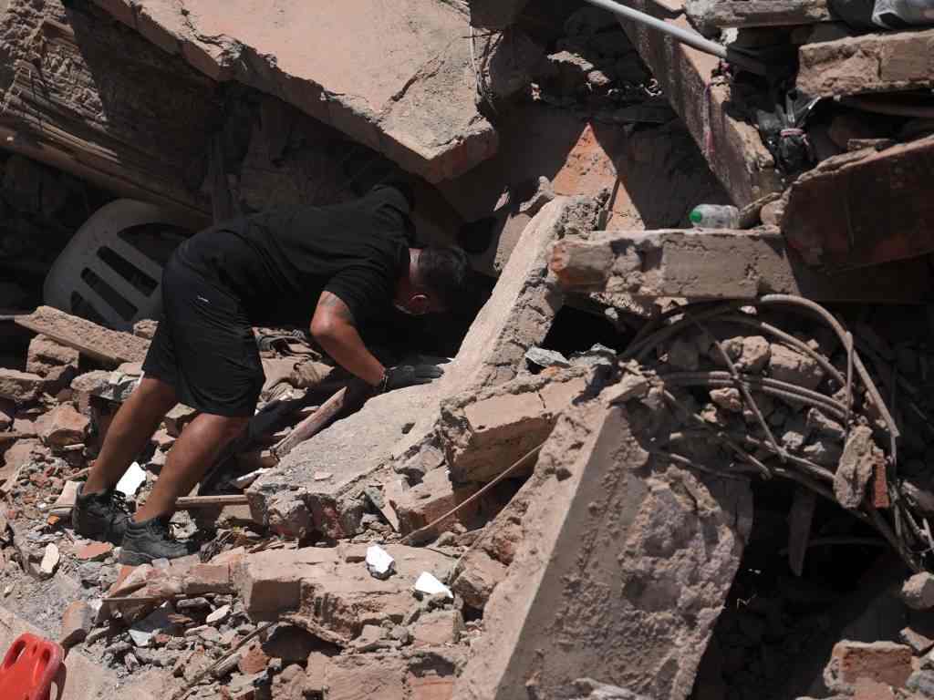 Hombre busca entre escombros de edificio colapsado por sismo.