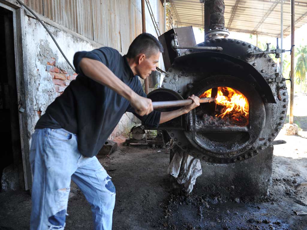 Hombre usando una barra de hierro para reavivar las llamas dentro del horno encendido de una caldera industrial de metal.