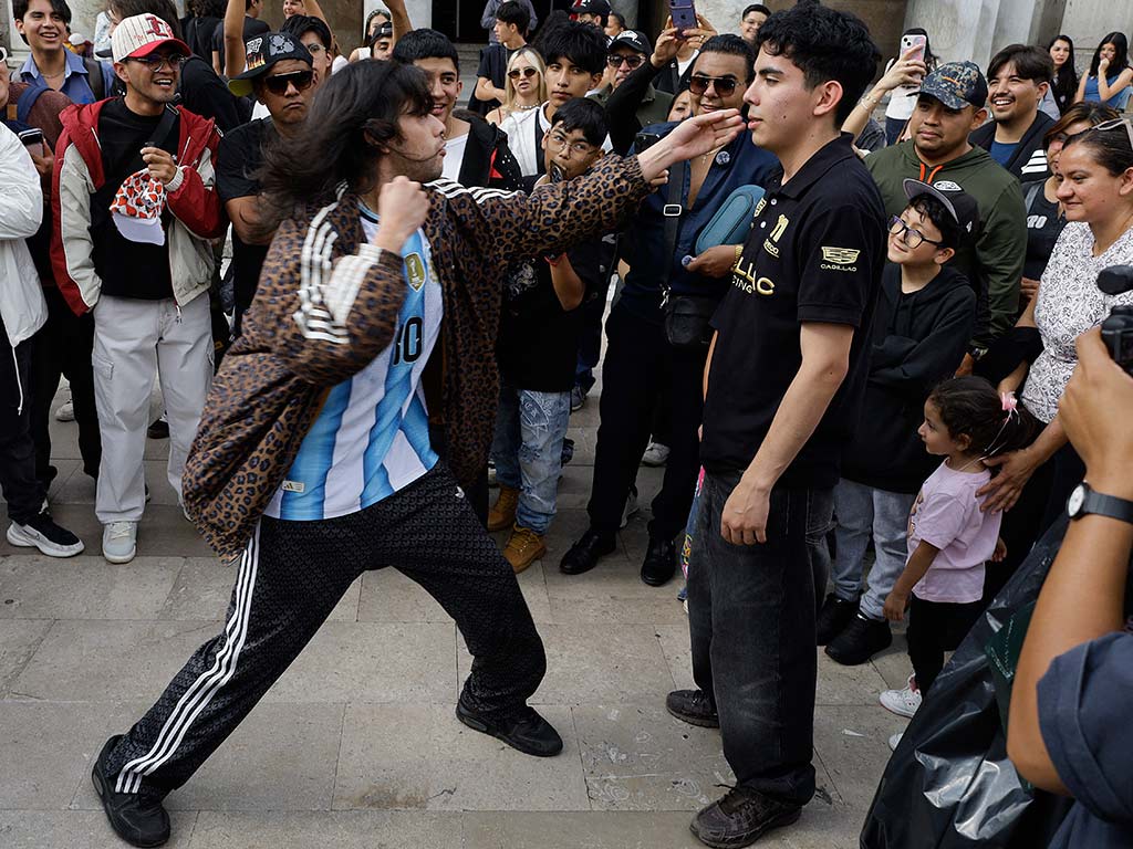 Un joven con chamarra de leopardo y camiseta de Argentina lanza un golpe al aire que se detiene muy cerca de la cara de otro competidor vestido de negro.