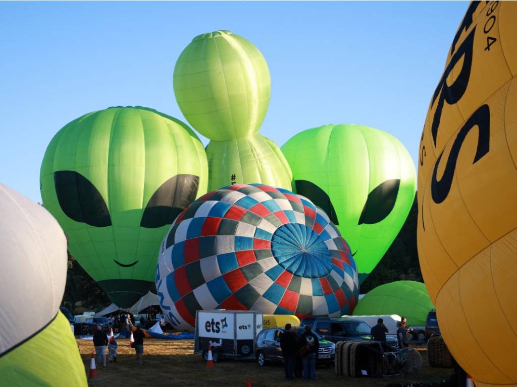 Globos aerostáticos verdes con diseño de extraterrestre inflados en el suelo antes de despegar.