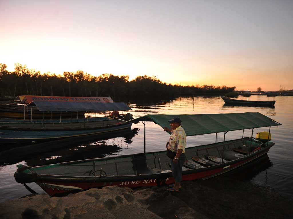 Lanchero junto a su barco de madera en el embarcadero durante la luz dorada del amanecer.