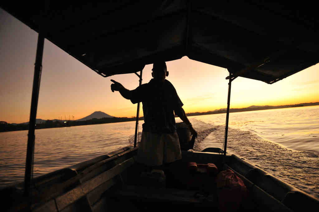 Silueta de un lanchero señalando hacia el horizonte al amanecer desde una embarcación en la Bahía de Jiquilisco.