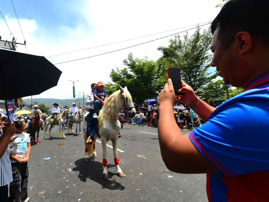Un padre toma una foto a su hija montada en un caballo del desfile.