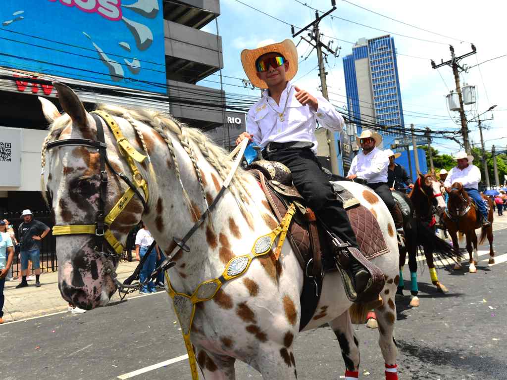 Un joven jinete saluda sonriente sobre un bello caballo moteado.