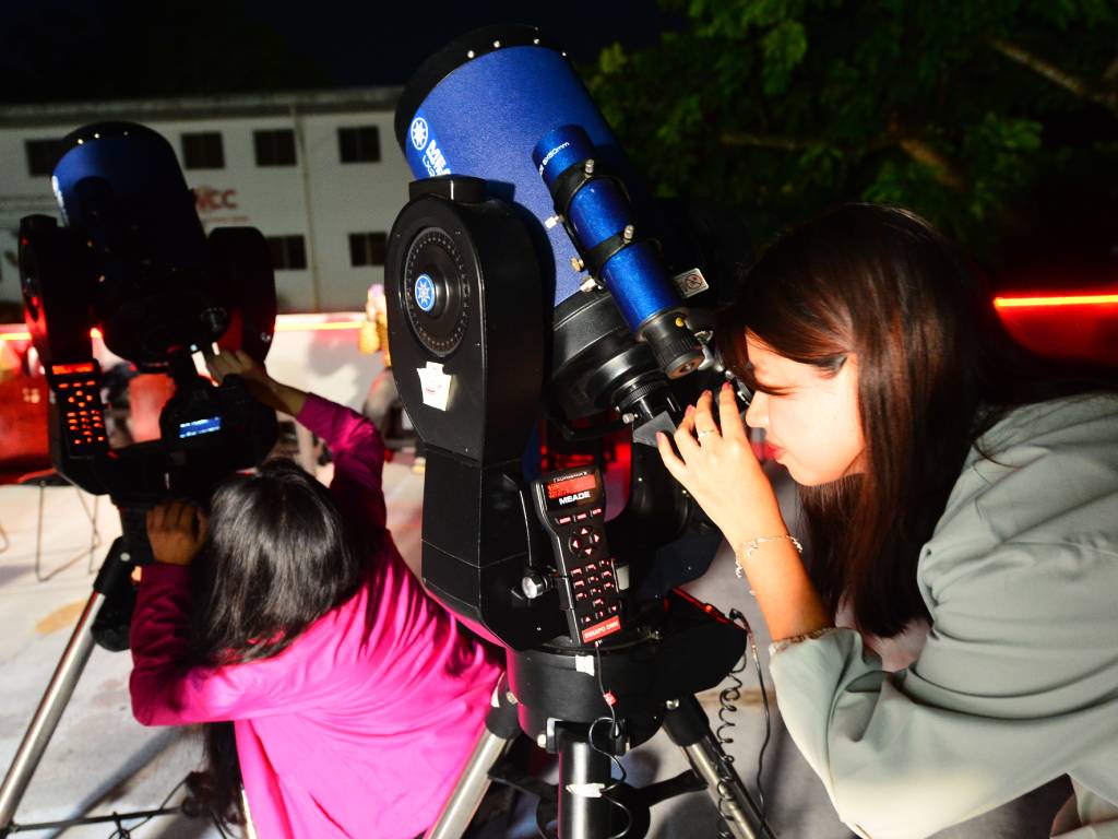 Personas agrupadas al aire libre junto a telescopios mirando con atención hacia el cielo nocturno.