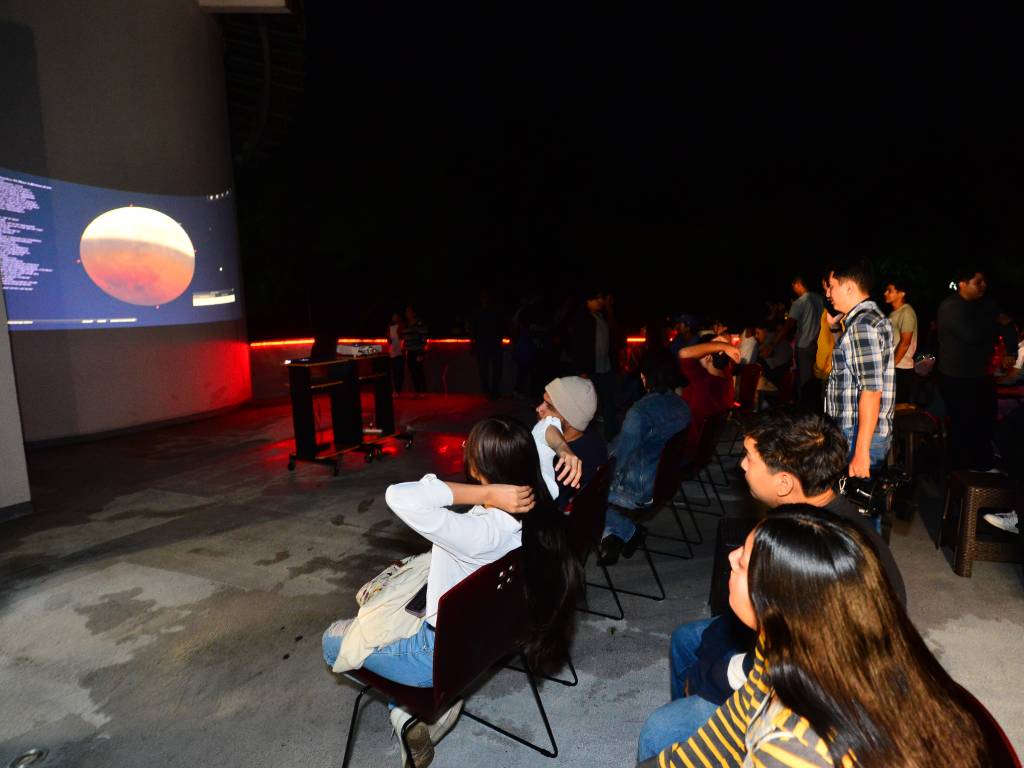 Personas mirando una pantalla grande que transmite en directo las fases de un eclipse astronómico.