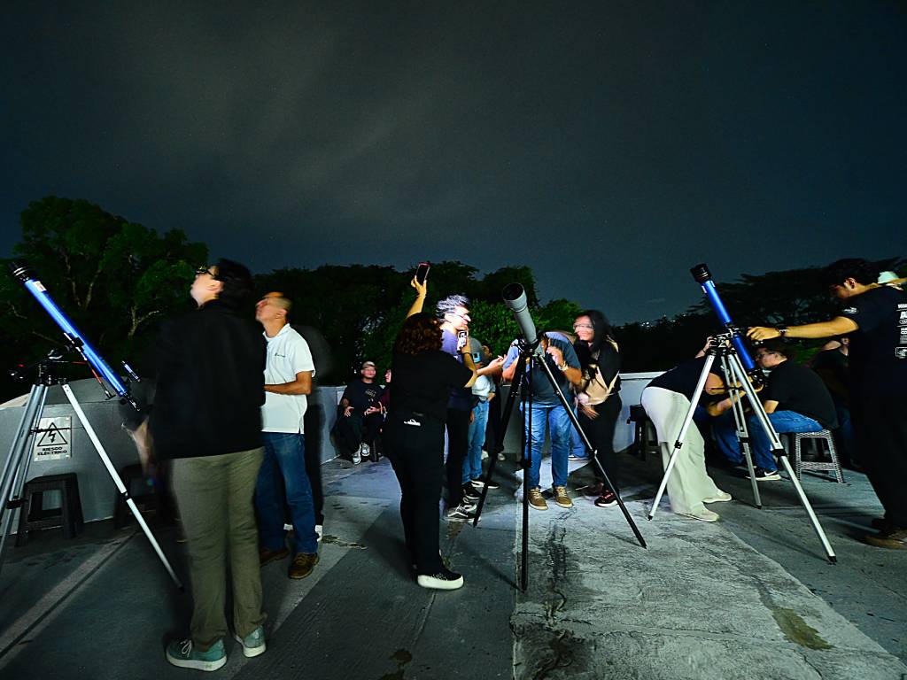 Grupo de personas reuniéndose al aire libre para mirar al cielo nocturno con telescopios durante la noche.