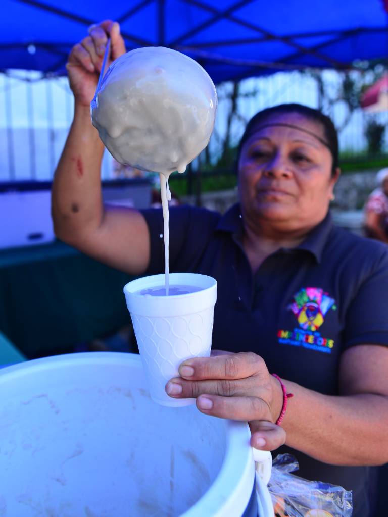 Silvia Flores sonríe mientras sirve atol de anona caliente en una taza a un visitante del festival.