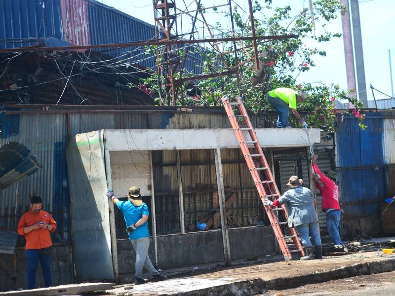 Grupo de trabajadores utilizando escaleras y herramientas para desmantelar una caseta comercial en la vía pública.