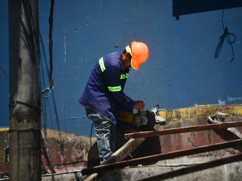 Trabajador corta con pulidora el armazón de hierro de un local comercial, generando chispas sobre la estructura metálica.
