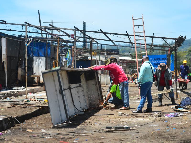 Operario cortando con una pulidora metal sobre la calle, produciendo chispas mientras otros trabajadores remueven estructuras