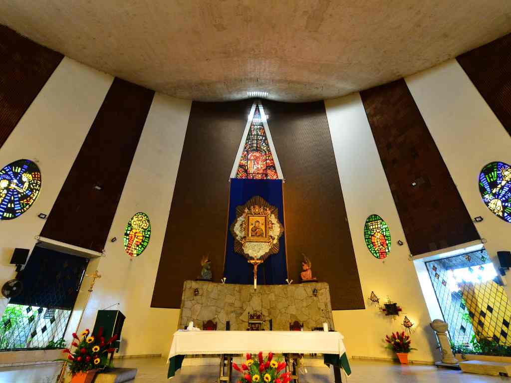 ista frontal del altar mayor con una mesa vestida de blanco, arreglos de flores y un cuadro iluminado en la pared principal.