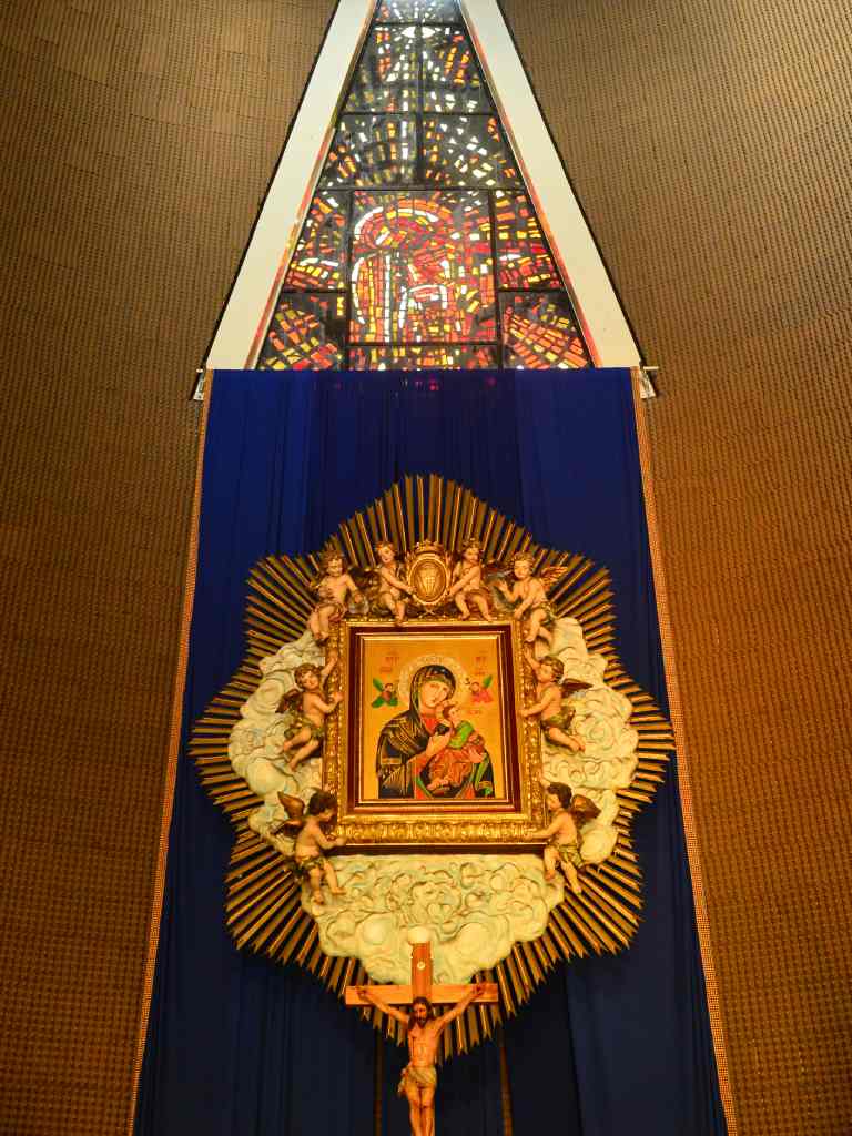 Vista frontal del retablo del altar mayor con un gran icono dorado de la Virgen y el Niño Jesús sobre un paño azul y debajo de una ventana de vitral triangular.