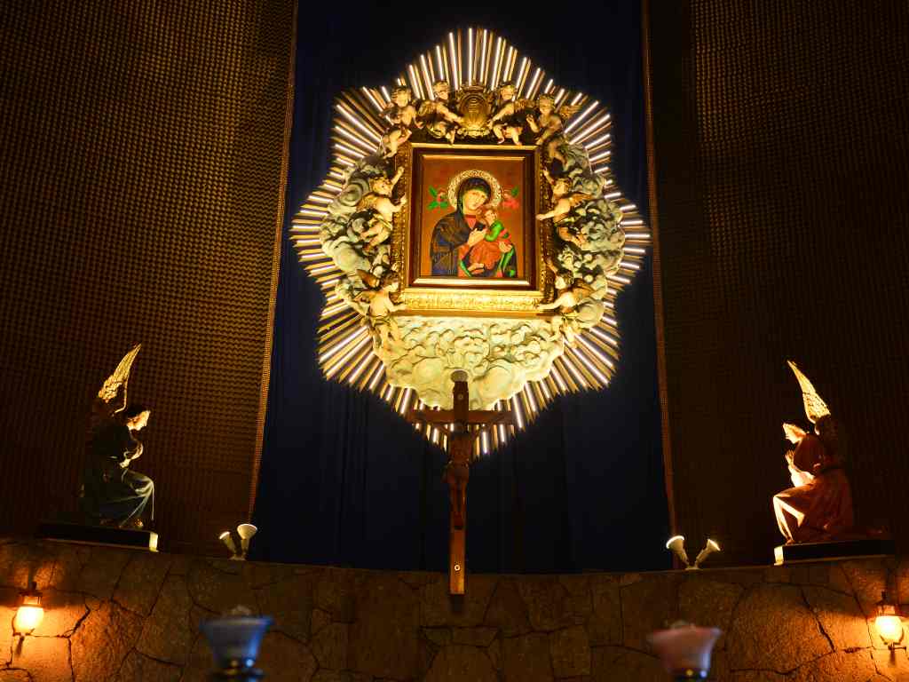 Plano detalle del cuadro de la Virgen con el Niño Jesús dentro de un Marco dorado rodeado de figuras de ángeles y rayos de luz.