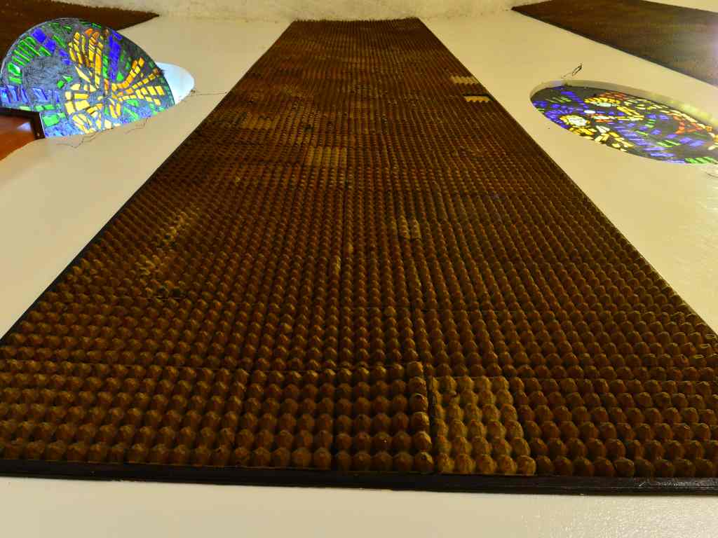 Contrapicado de una pared blanca con un panel marrón de cartón de huevo acústico flanqueado por vitrales circulares.