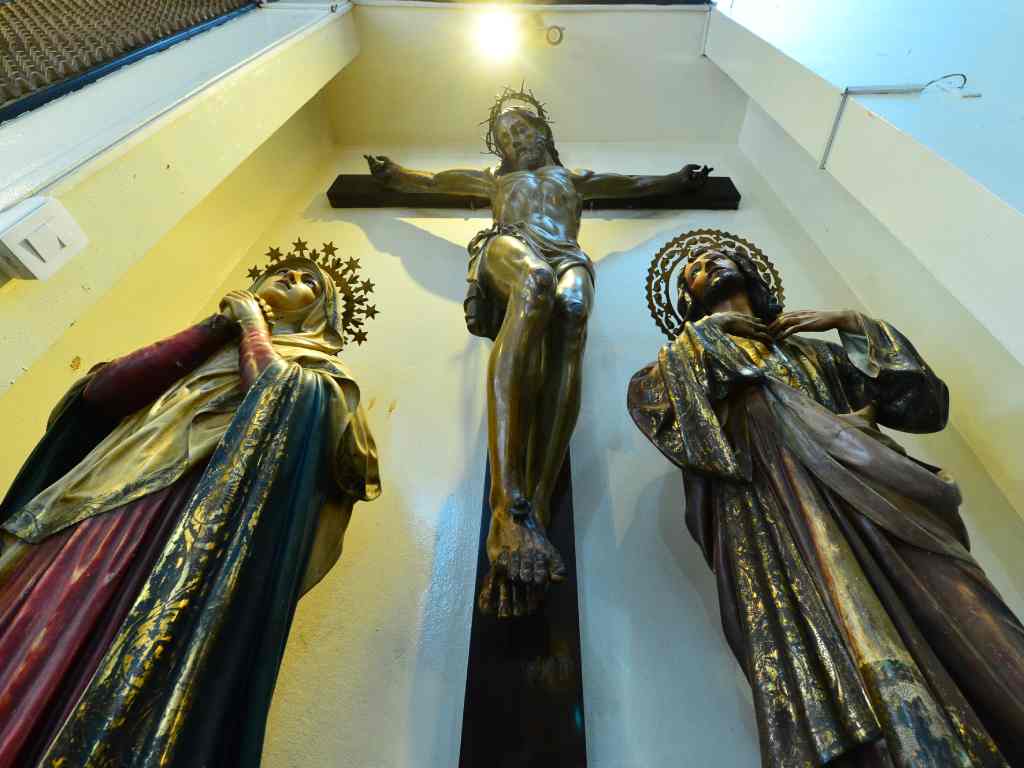 Contrapicado de tres esculturas religiosas: Cristo en la cruz al centro junto a la Virgen María y San Juan Evangelista.