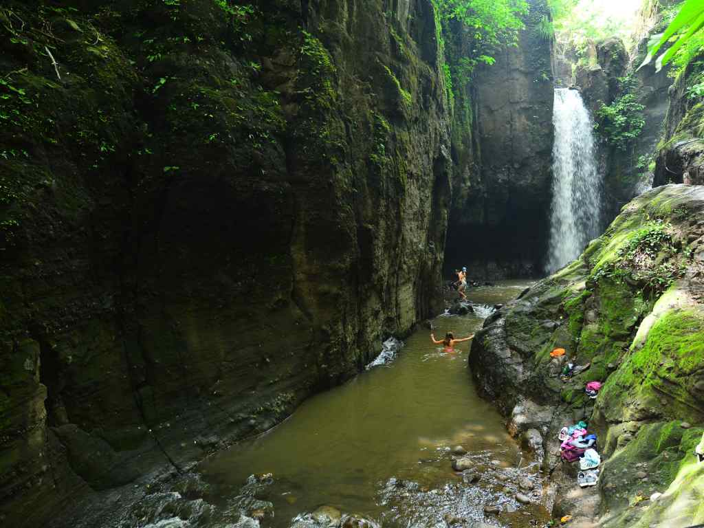 Personas nadando en una poza natural de agua cristalina rodeada de rocas.