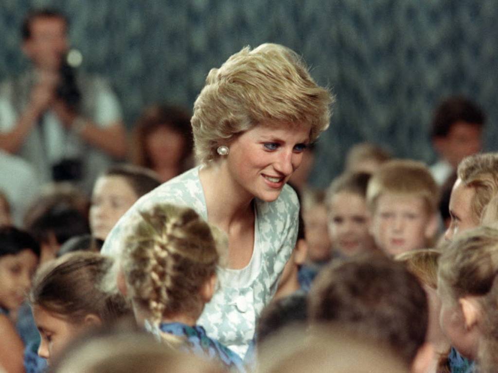 La princesa Diana de Gales agachada conversando sonriente con niños en la escuela internacional británica de Yakarta.