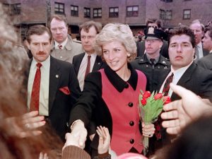 La princesa Diana de Gales sonriendo y saludando con la mano desde el palco real de un teatro neoyorquino.