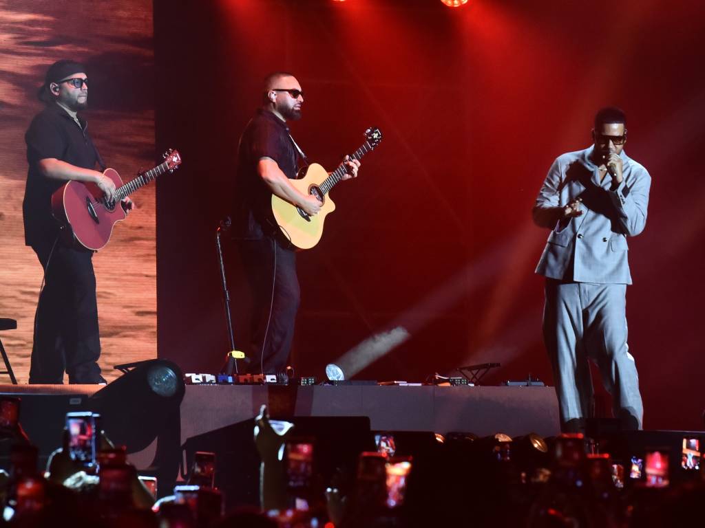 Romeo Santos cantando con micrófono en mano en el escenario frente a una multitud entusiasmada.