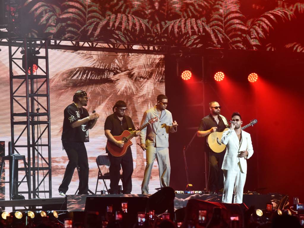 Romeo Santos y Prince Royce juntos en el escenario posando sonrientes bajo las luces del concierto.